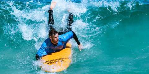 Man lies on an orange surfboard in the ocean