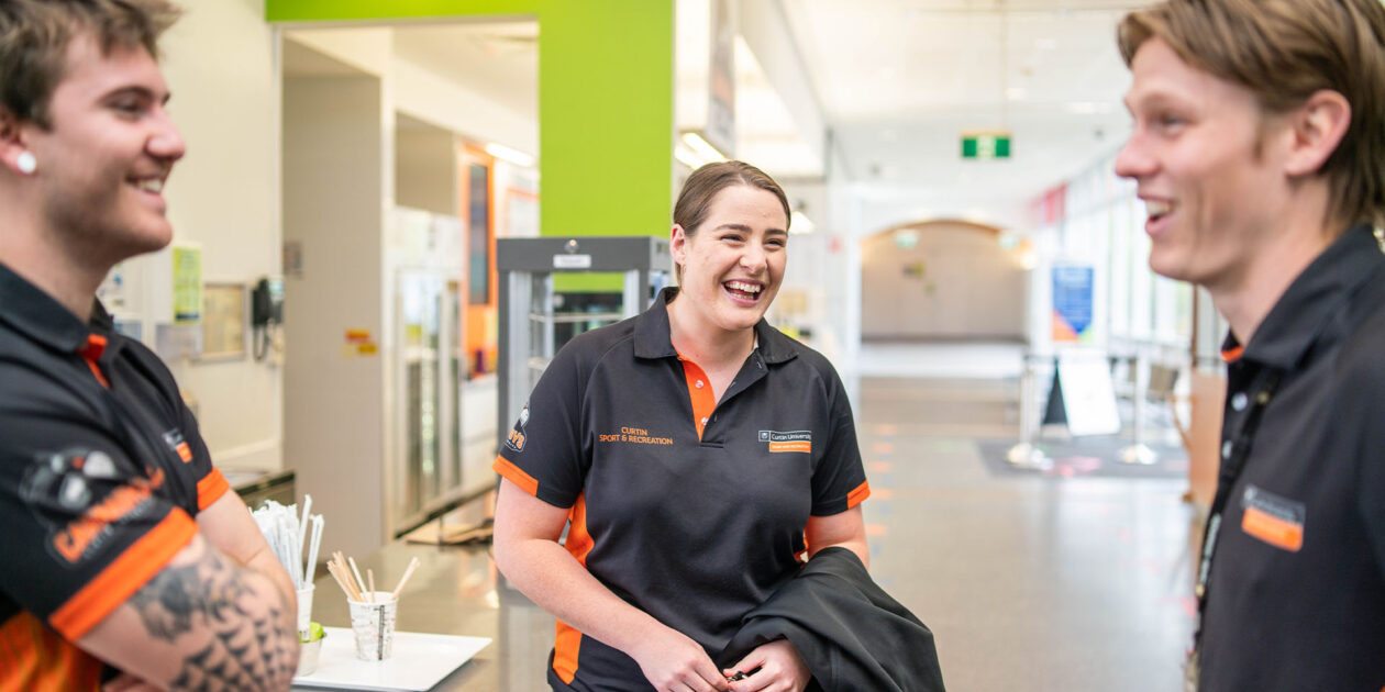Three Curtin Stadium staff members laugh while talking to each other